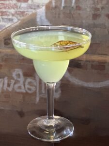 A classic margarita cocktail - a frosty glass with a salt-rimmed edge, filled with a vibrant lime-green liquid, featuring tequila, triple sec, and lime juice, garnished with a lime wedge. A tangy and refreshing drink perfect for fiestas and happy hours