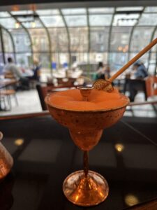 Chilled and icy delight with a burst of citrus - Frozen Margarita in special hand made cupper cup , featuring a slushy blend of tequila, lime juice, triple sec, and ice. Garnished with a lime wheel. A refreshing and tangy treat perfect for warm weather sipping